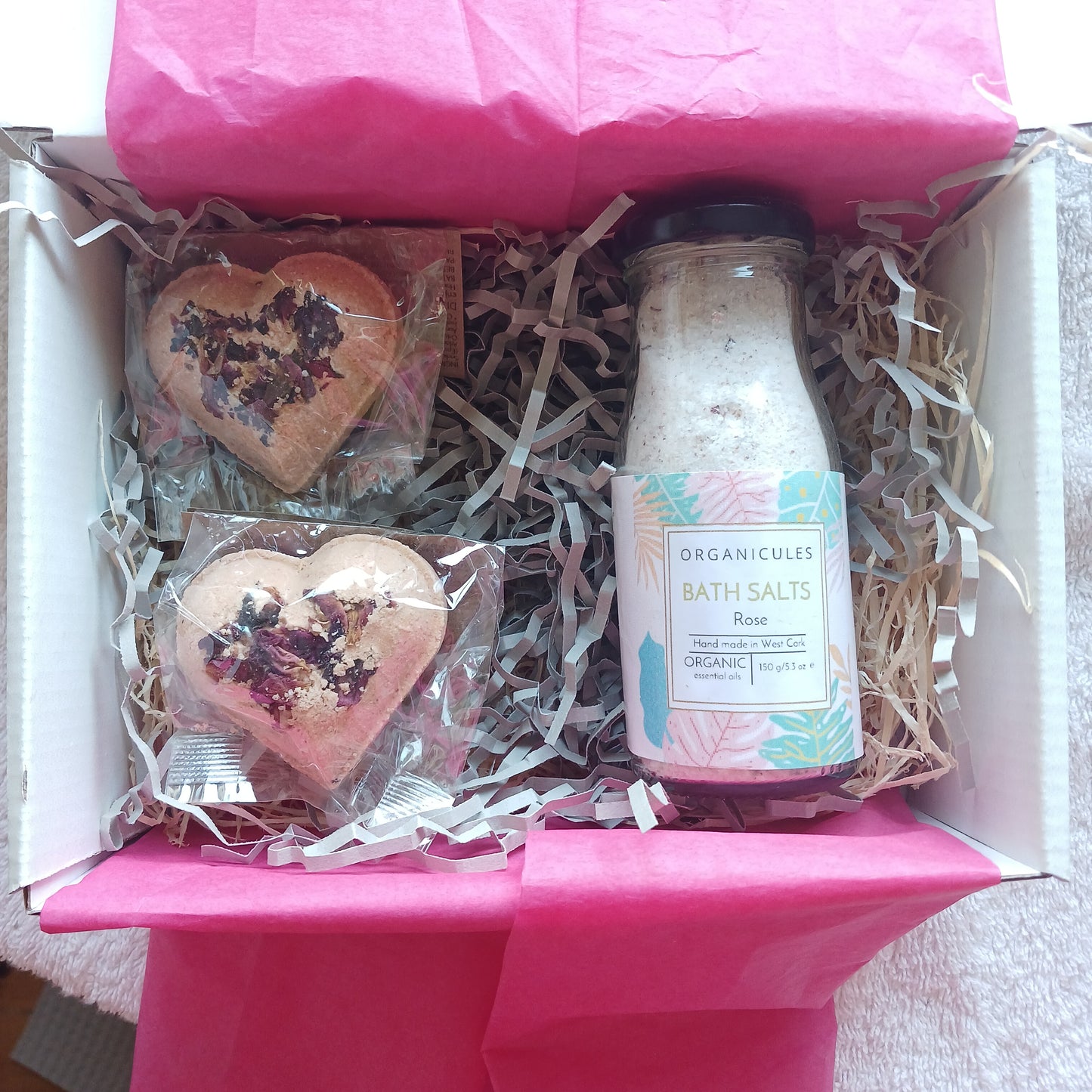Contents of rose infused gift box by organicules containing a bottle of rose bath salts and two pink clay bath bombs